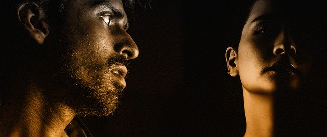 faces of a man and a woman facing different directions in the darkness